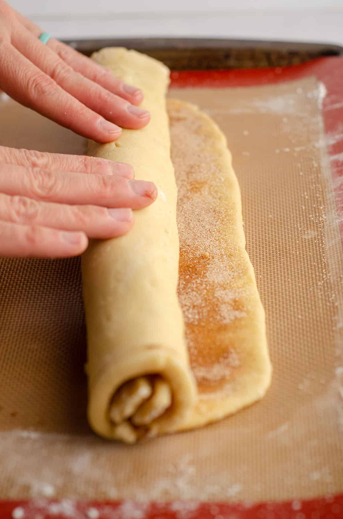 hands rolling up cinnamon pinwheel cookie dough
