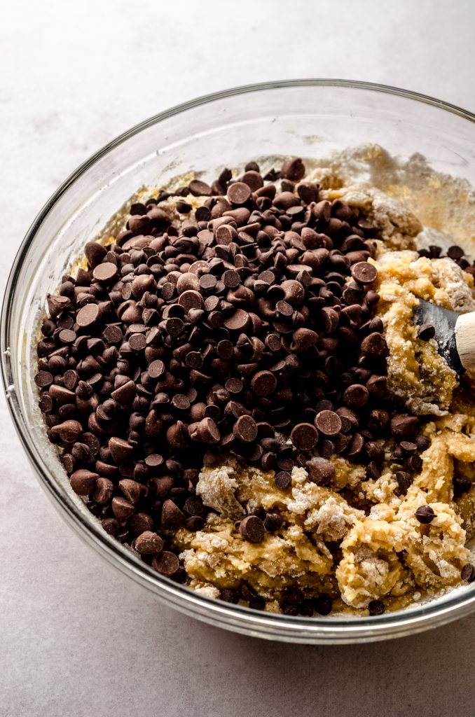 Chocolate chips added to chocolate chip cookie dough in a bowl with a spatula.