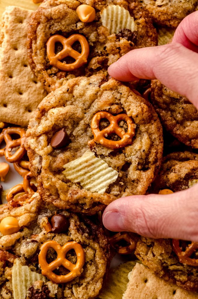 Someone is holding a compost cookie surrounded by pretzels, chips, and graham cracker pieces.
