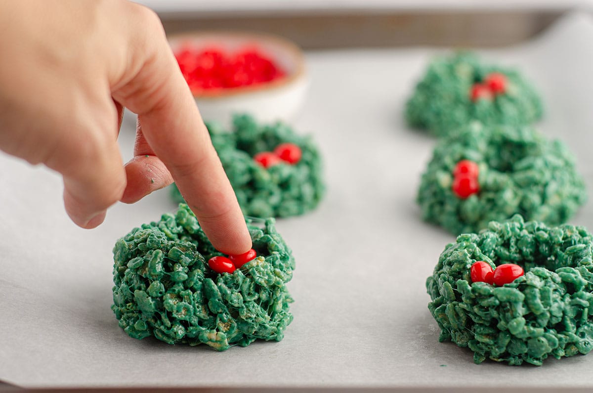 hand placing red candies on rice krispies wreath