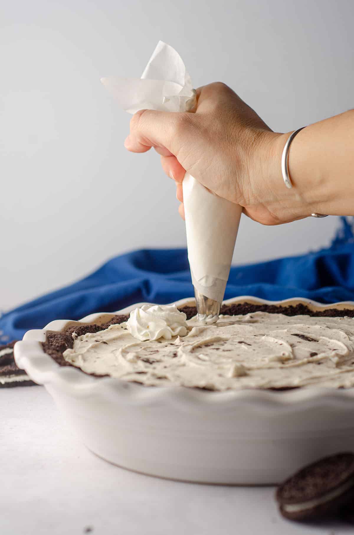 hand piping homemade whipped cream onto the top of no bake oreo pie
