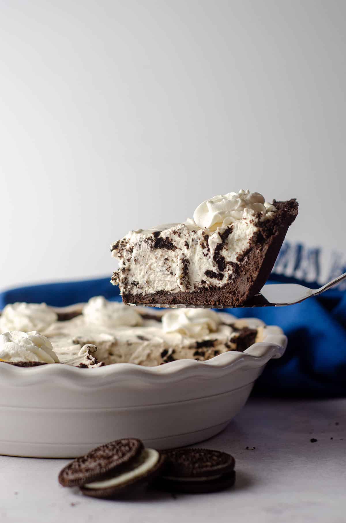 slice of no bake oreo pie sitting on a pie server hovering over the rest of the pie in a pie plate