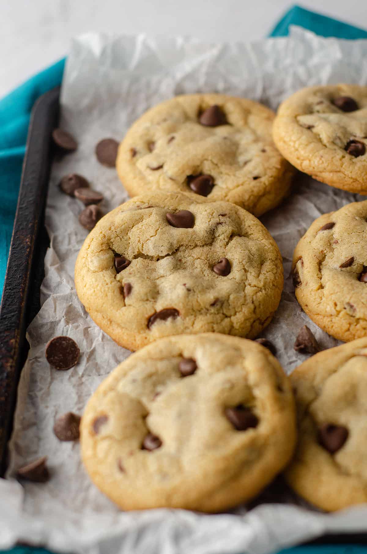 small batch of 6 chocolate chip cookies sitting on parchment paper on a baking sheet