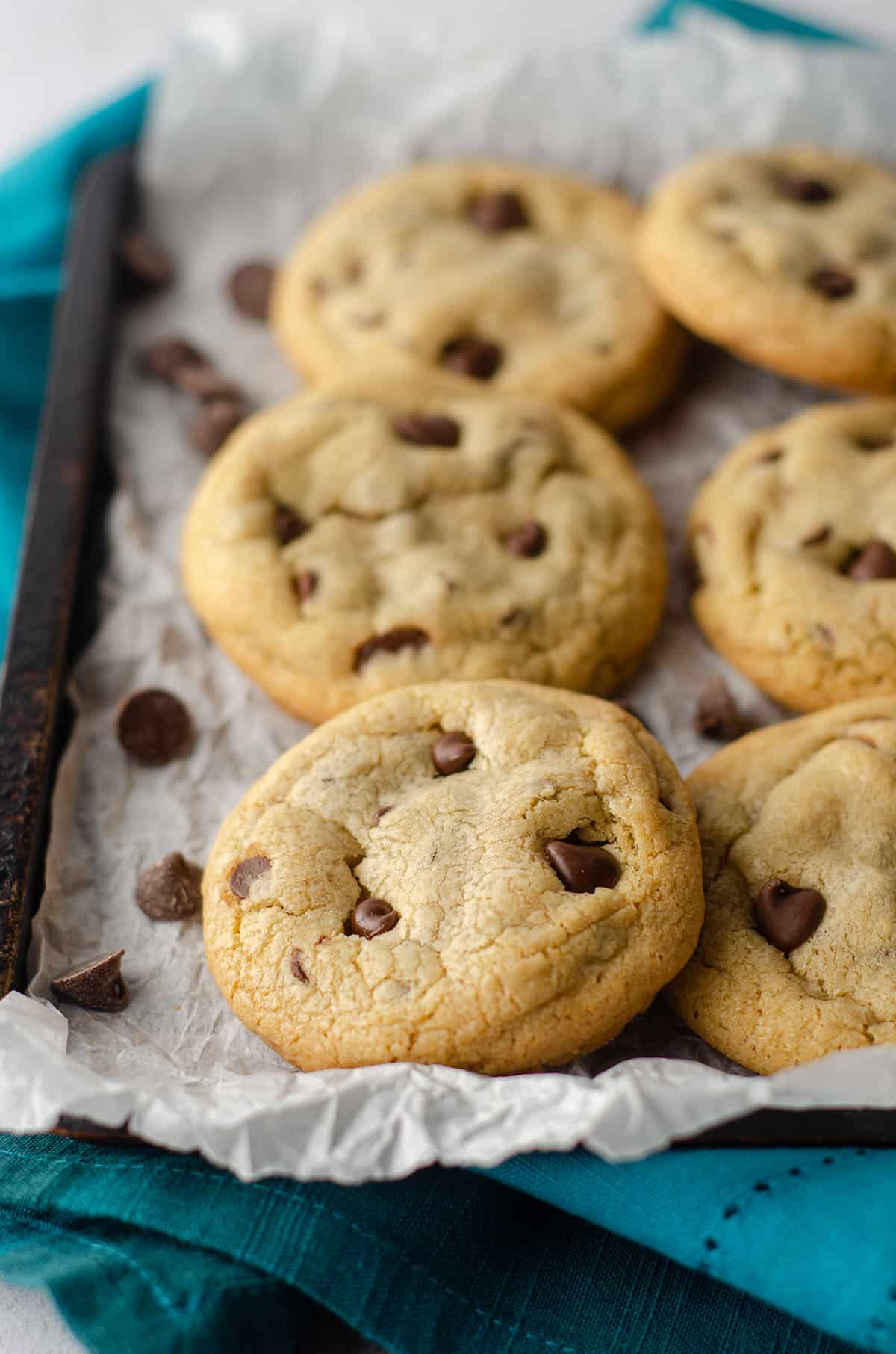 small batch of 6 chocolate chip cookies sitting on parchment paper on a baking sheet