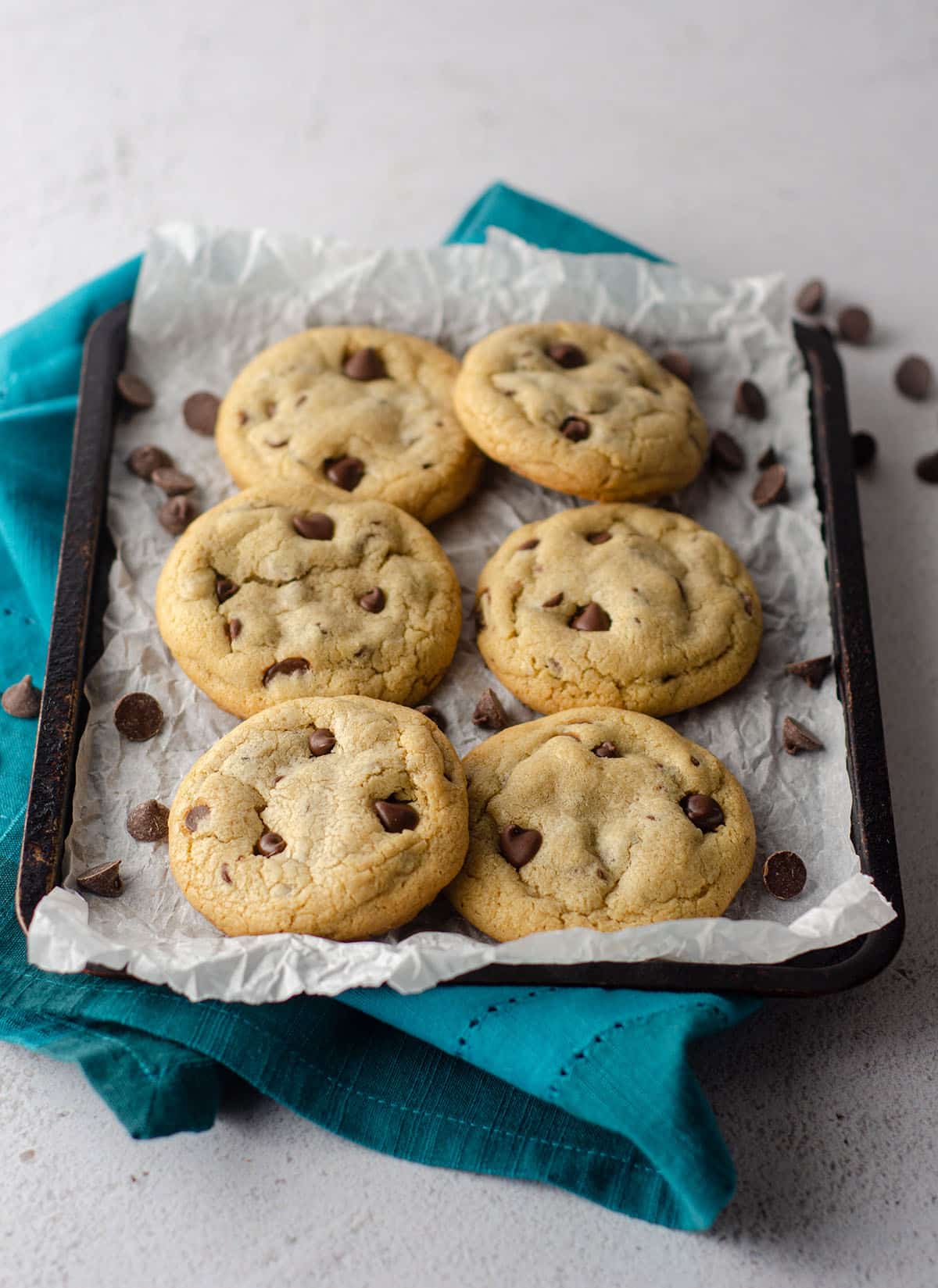 small batch of 6 chocolate chip cookies sitting on parchment paper on a baking sheet