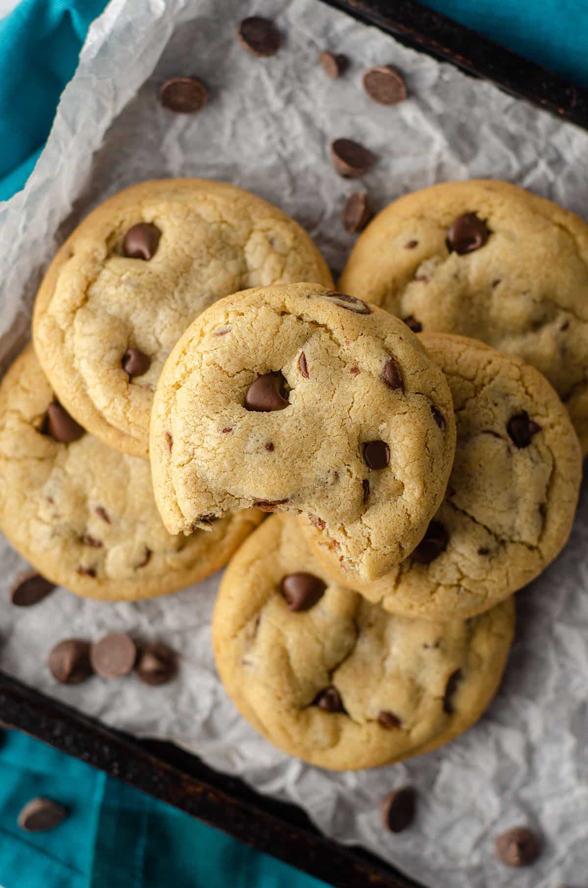 aerial photo of 6 small batch chocolate chip cookies sitting on parchment paper on a baking sheet and a bite is taken out of the one on the top