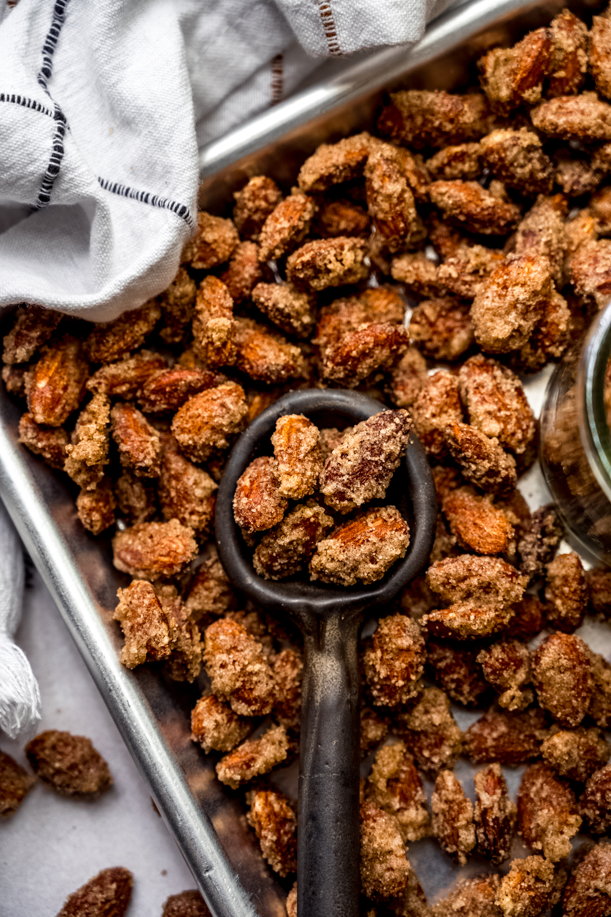 Aerial photo of a serving spoon scooping up candied almonds from a baking sheet.