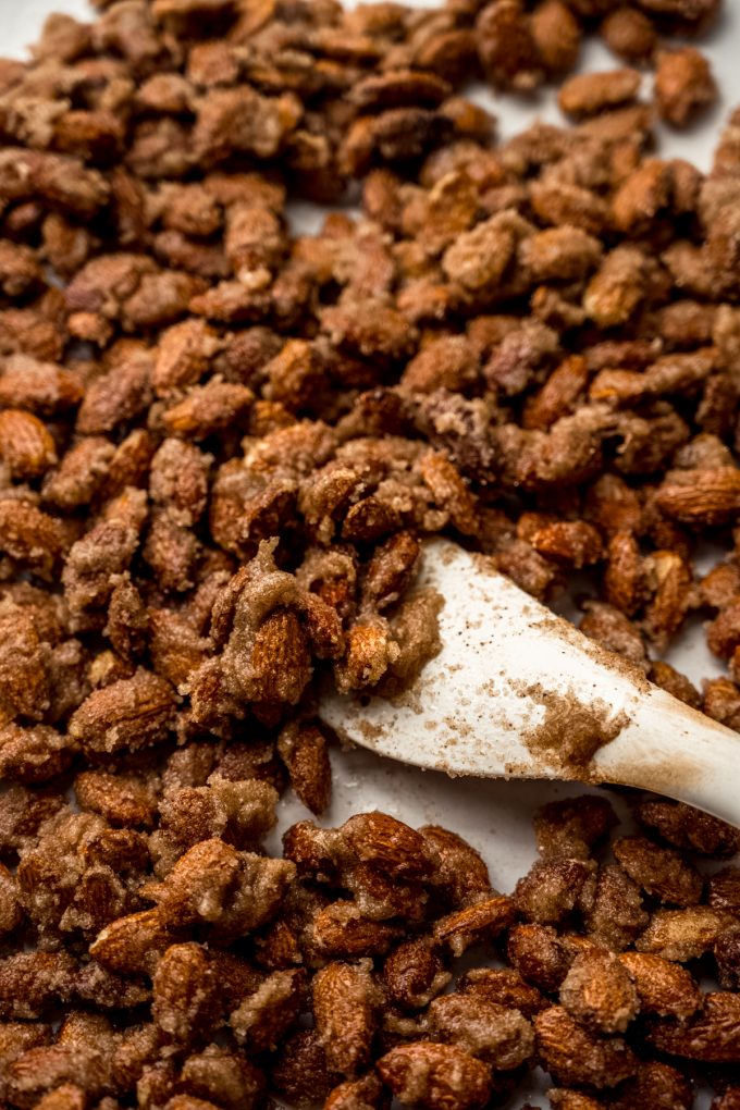 Someone is using a spatula to spread candied almonds onto a baking sheet.