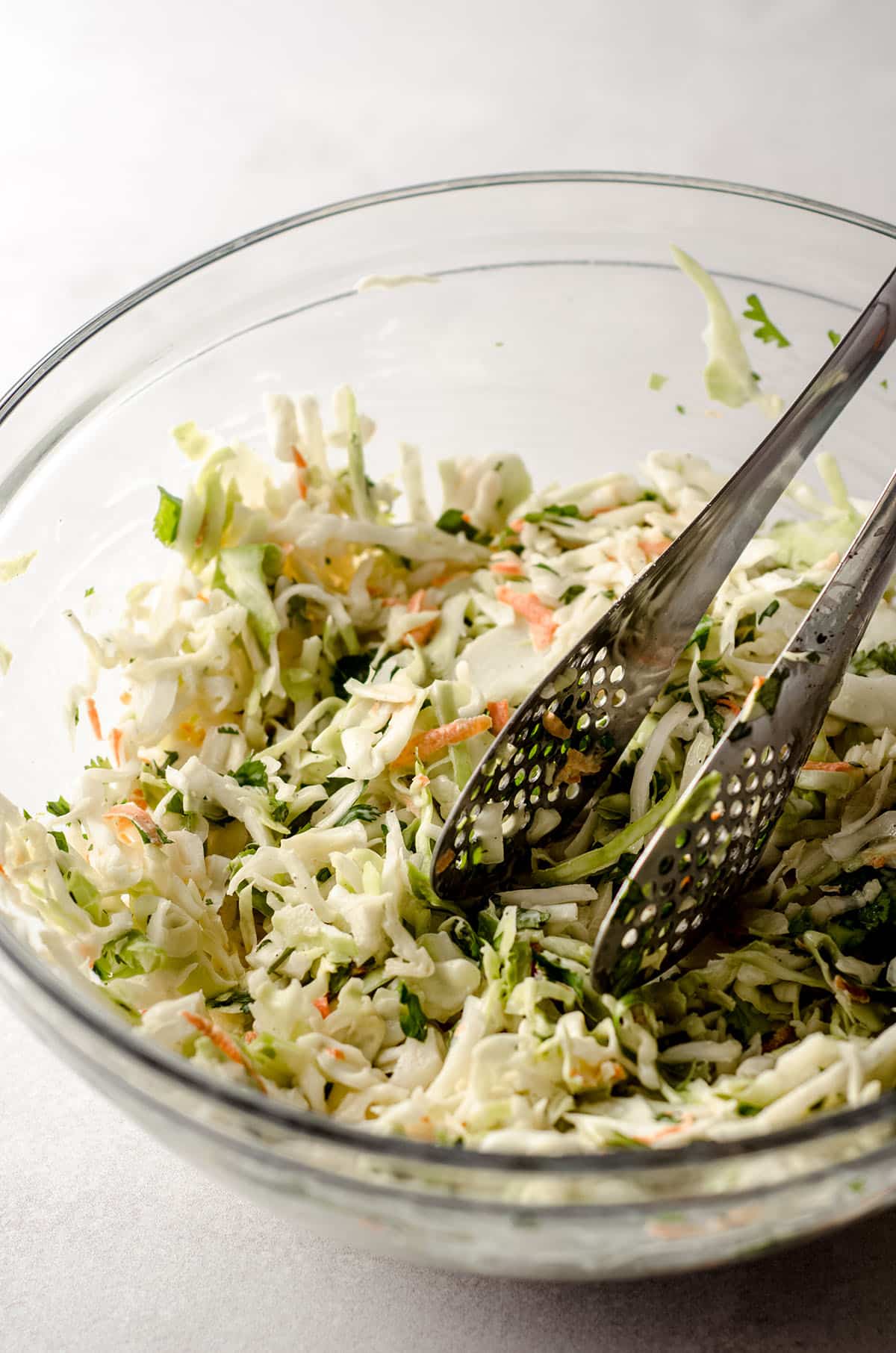 cilantro slaw in a glass bowl with metal tongs for serving