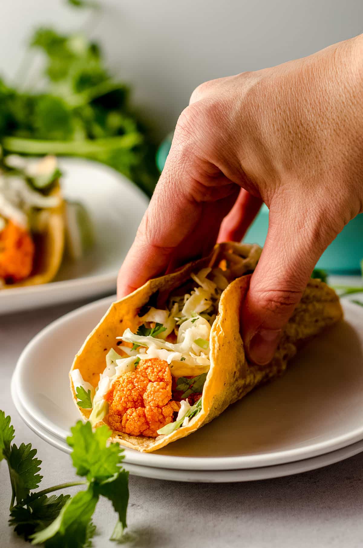 a hand grabbing a buffalo cauliflower taco from a white plate