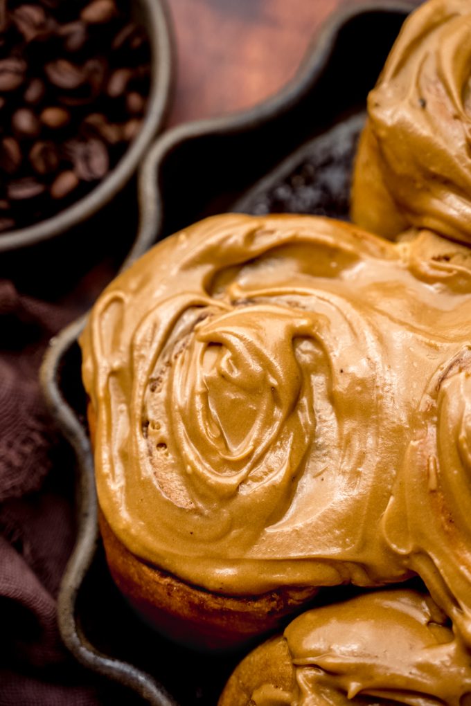 Coffee cinnamon rolls in a dish with a small bowl of coffee beans in the background.