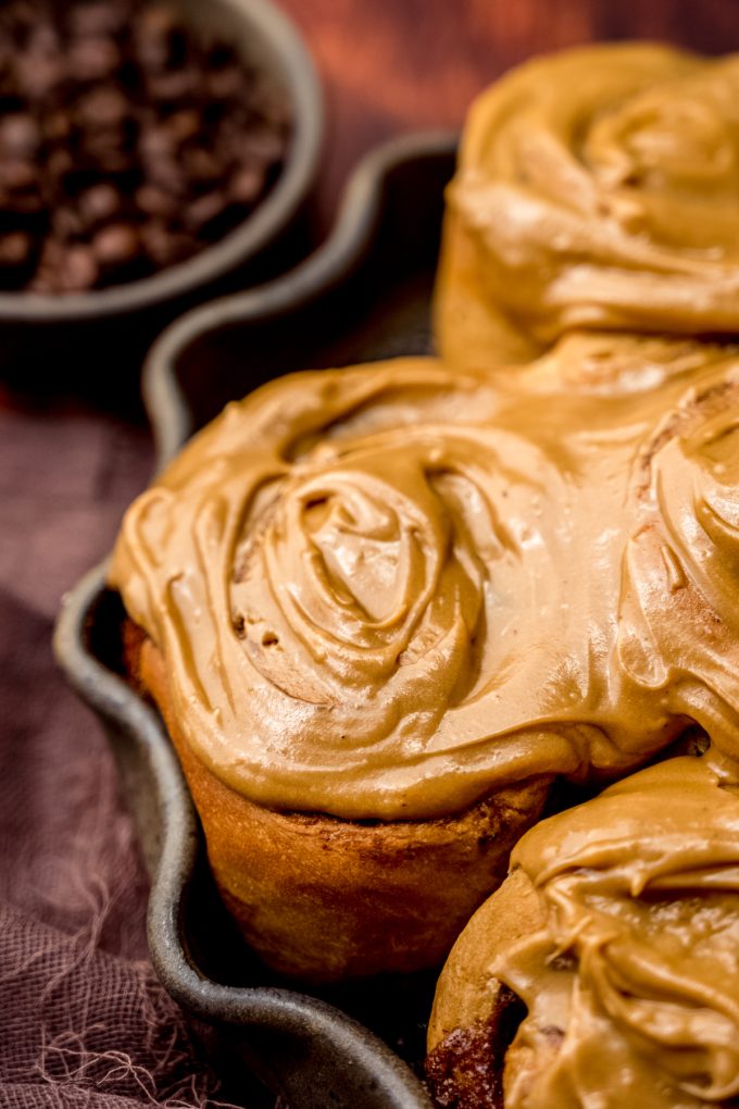 Coffee cinnamon rolls in a dish with a small bowl of coffee beans in the background.