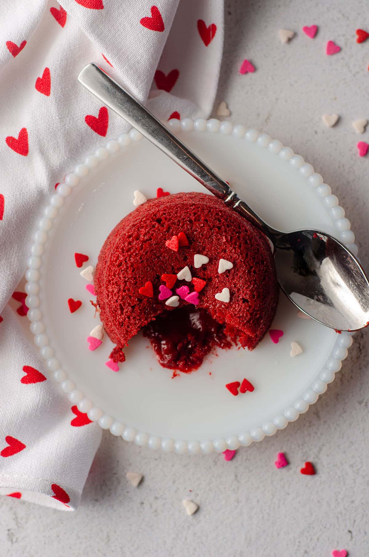 aerial photo of red velvet lava cake sitting on a white plate with heart sprinkles on top of it