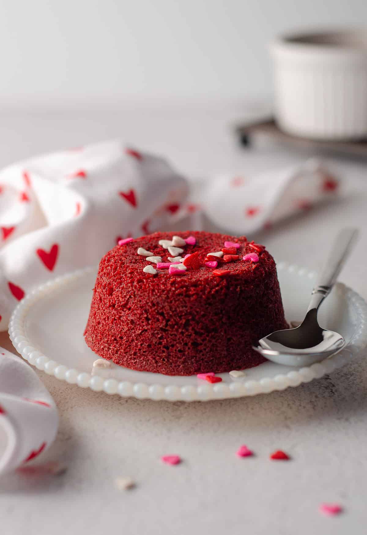 red velvet lava cake sitting on a white plate with a spoon and decorated with mini heart sprinkles