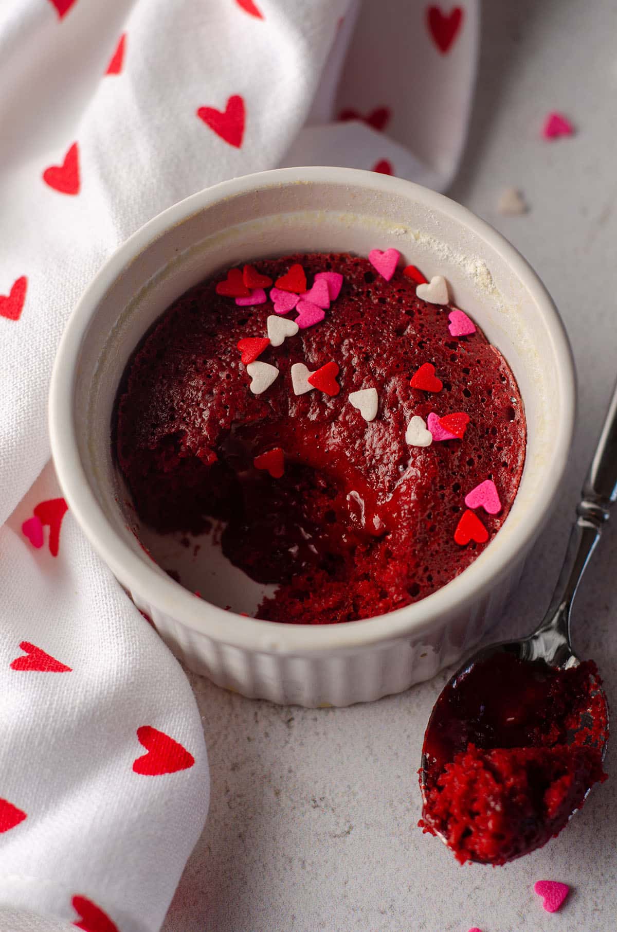red velvet lava cake in a white ramekin with pink, red, and white heart sprinkles on it