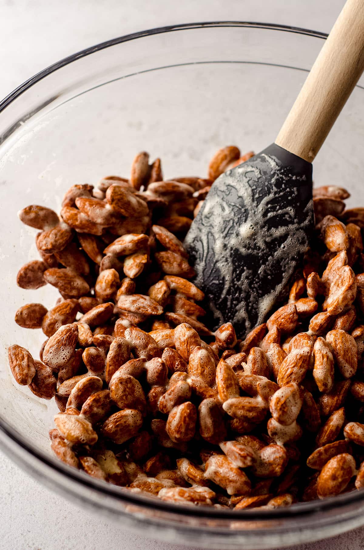 almonds in a glass bowl coated with vanilla paste and frothed egg whites to make candied almonds