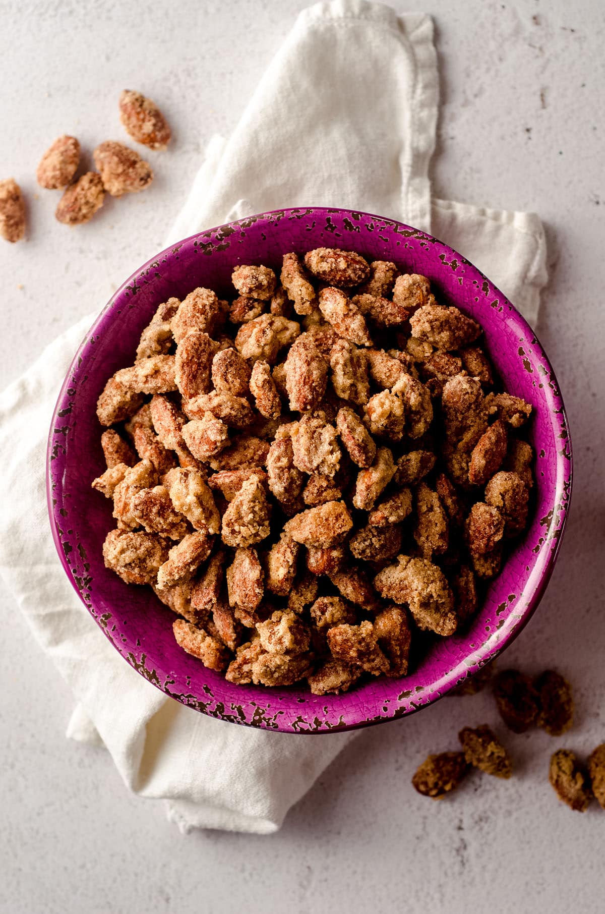 aerial photo of candied almonds in a plum colored bowl with a white kitchen towel