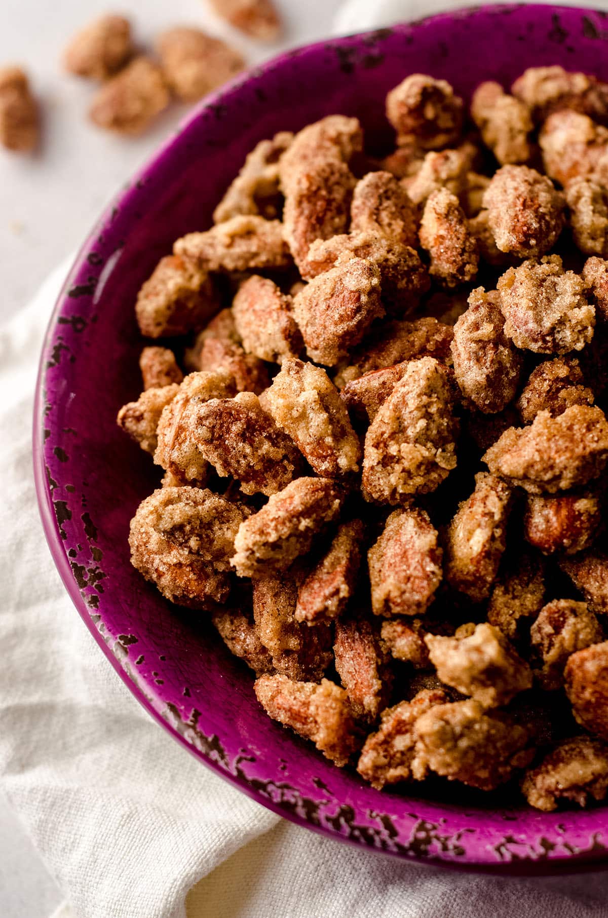 candied almonds in a plum colored bowl with a white kitchen towel