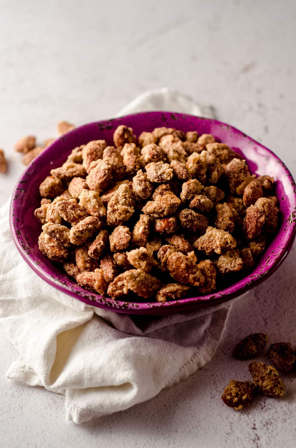 candied almonds in a plum colored bowl with a white kitchen towel