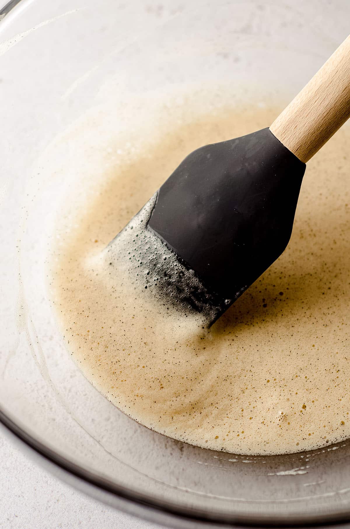 frothed egg whites with specks of vanilla bean in a glass bowl with a gray spatula