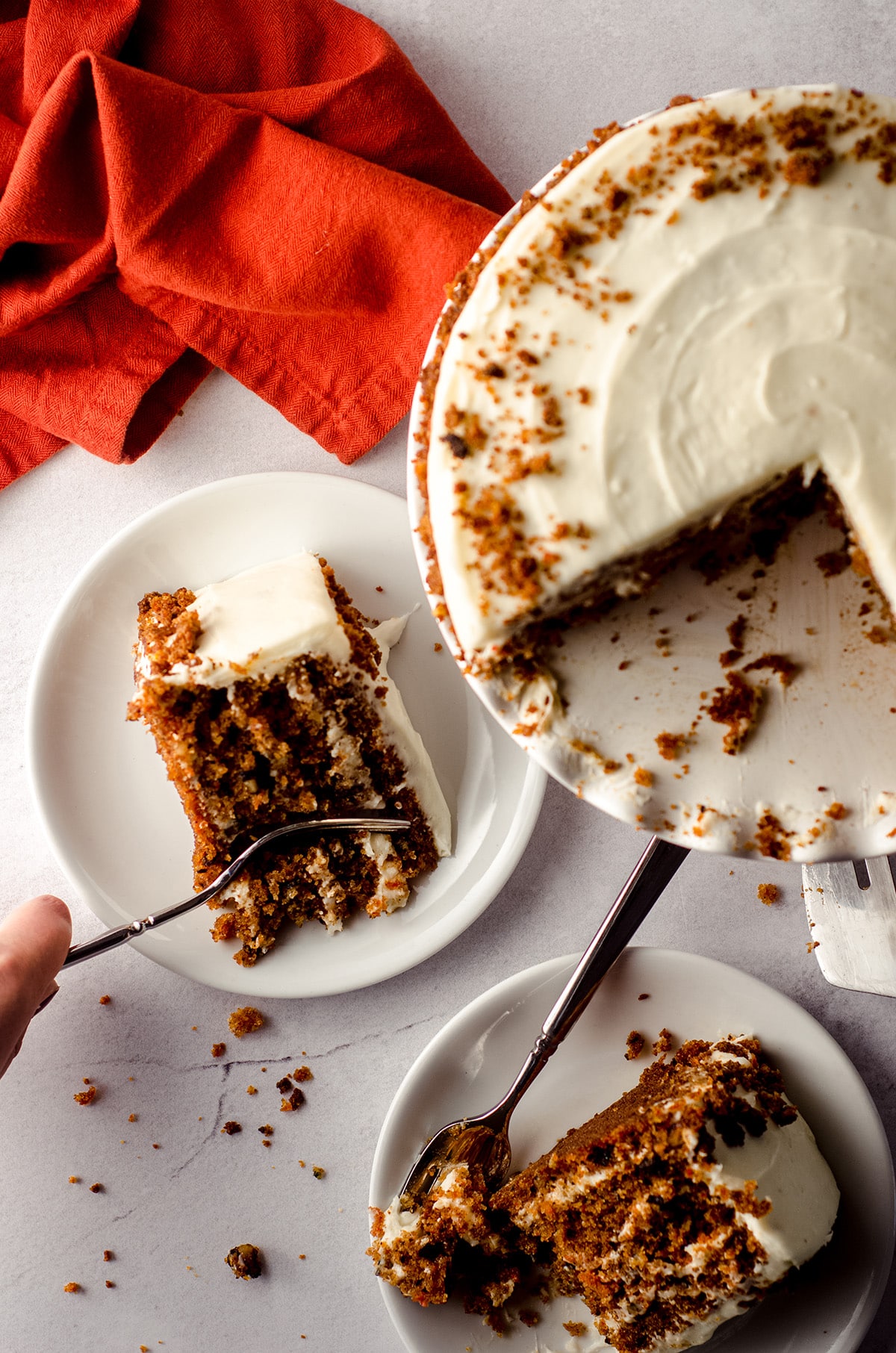 aerial photo of two slices of carrot walnut cake on plates and one has a fork digging into it for a bite