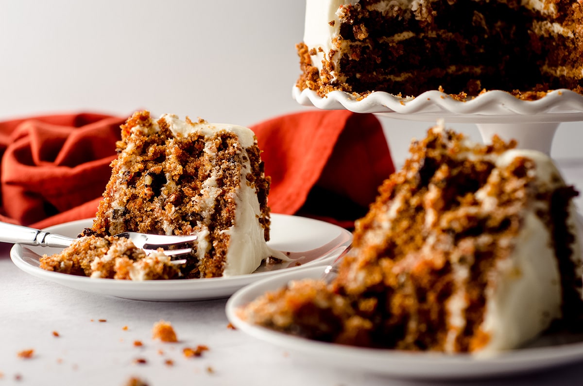 two slices of carrot walnut cake on plates and one has a fork digging into it