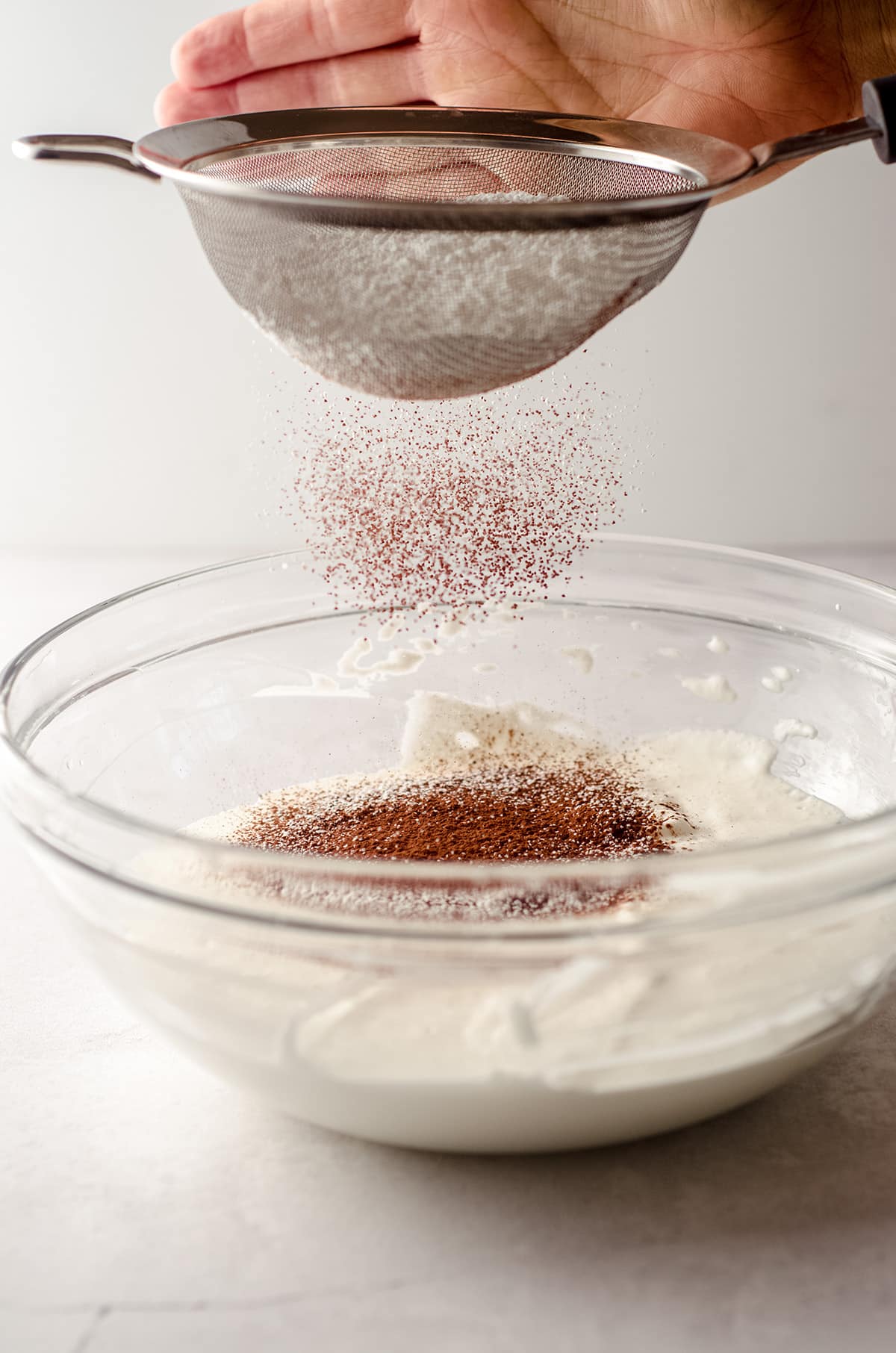 sifting cocoa powder and powdered sugar into whipped cream to make easy chocolate mousse