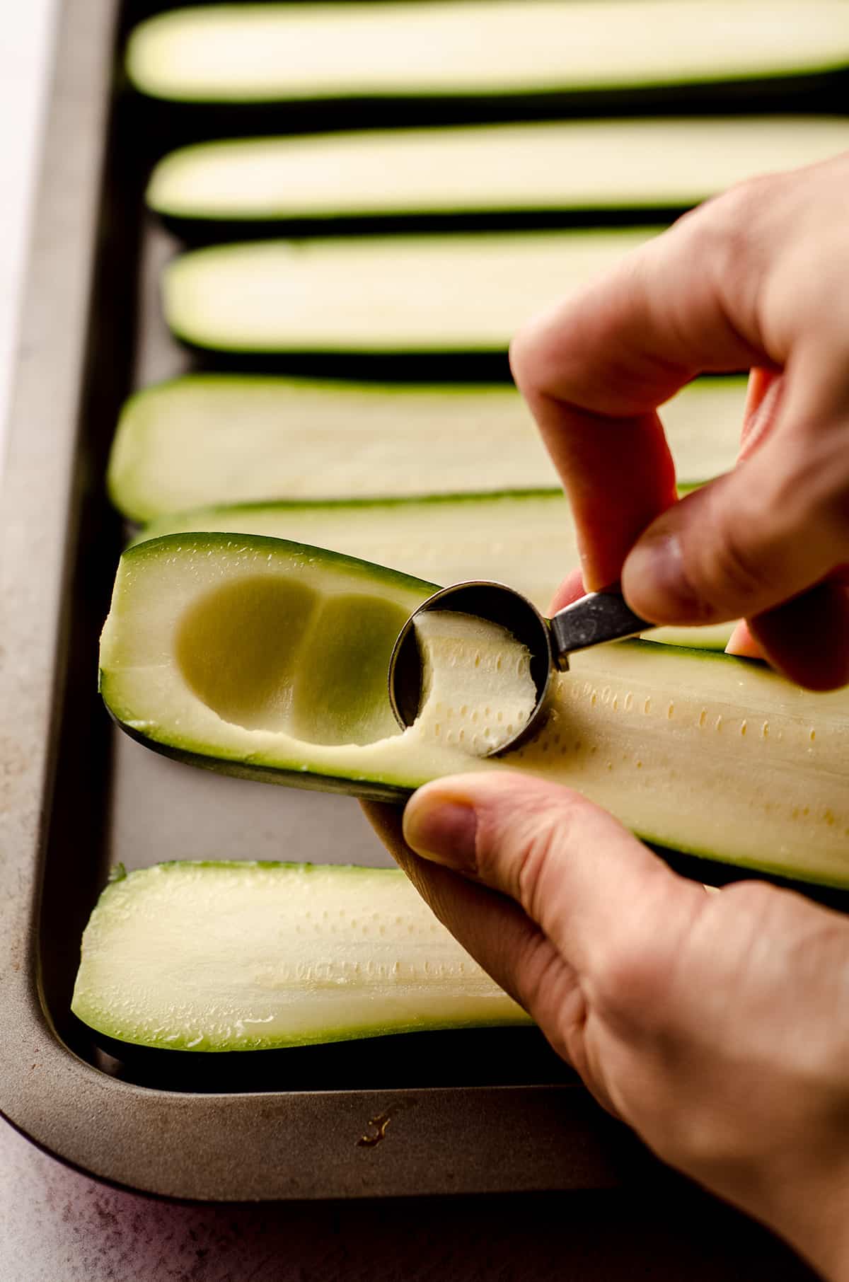 scooping out the insides of halved zucchini to make taco zucchini boats