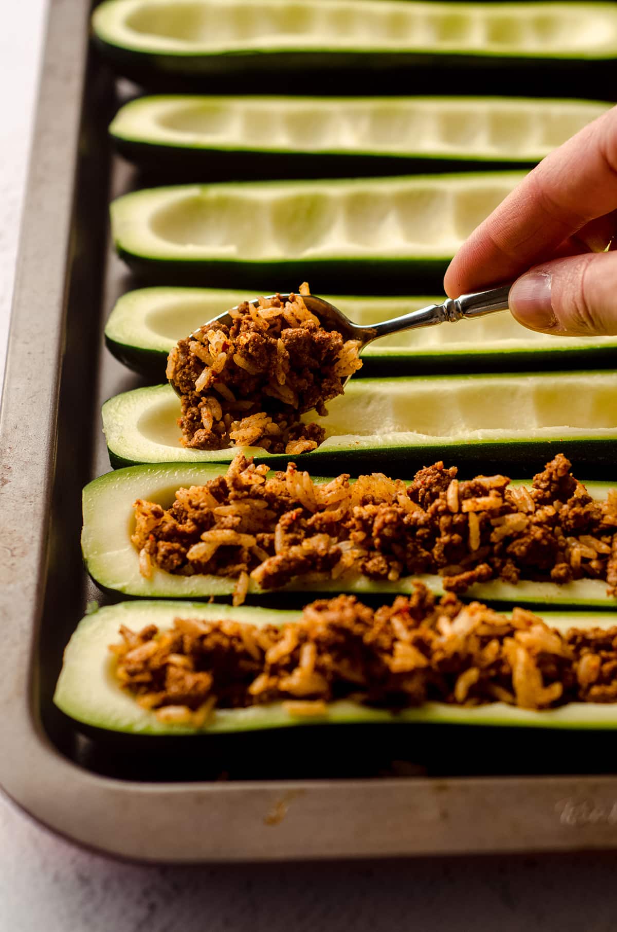 spoon putting filling into halved and seeded zucchini