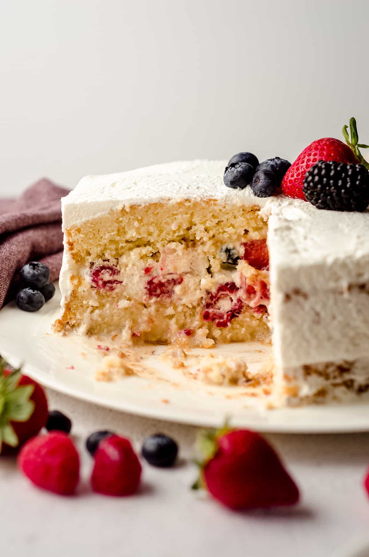 milk and berries cake on a plate with a slice taken out of it