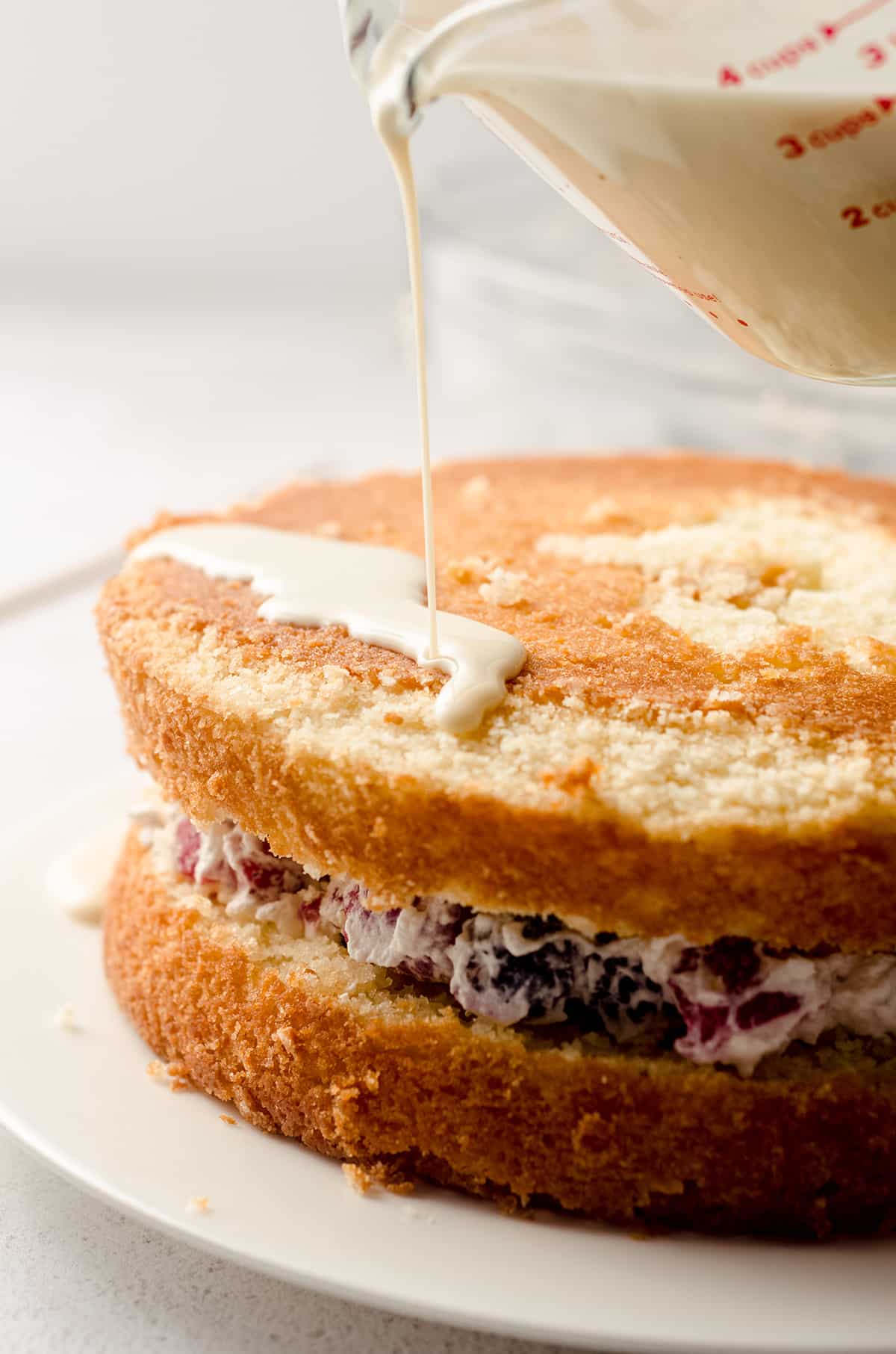 pouring tres leches syrup onto a milk and berries cake