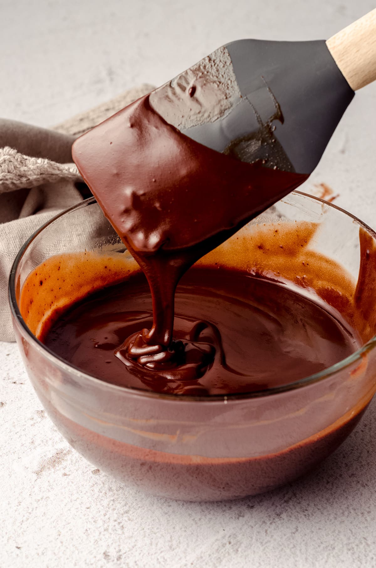 bowl of chocolate ganache with a spatula dripping into the bowl