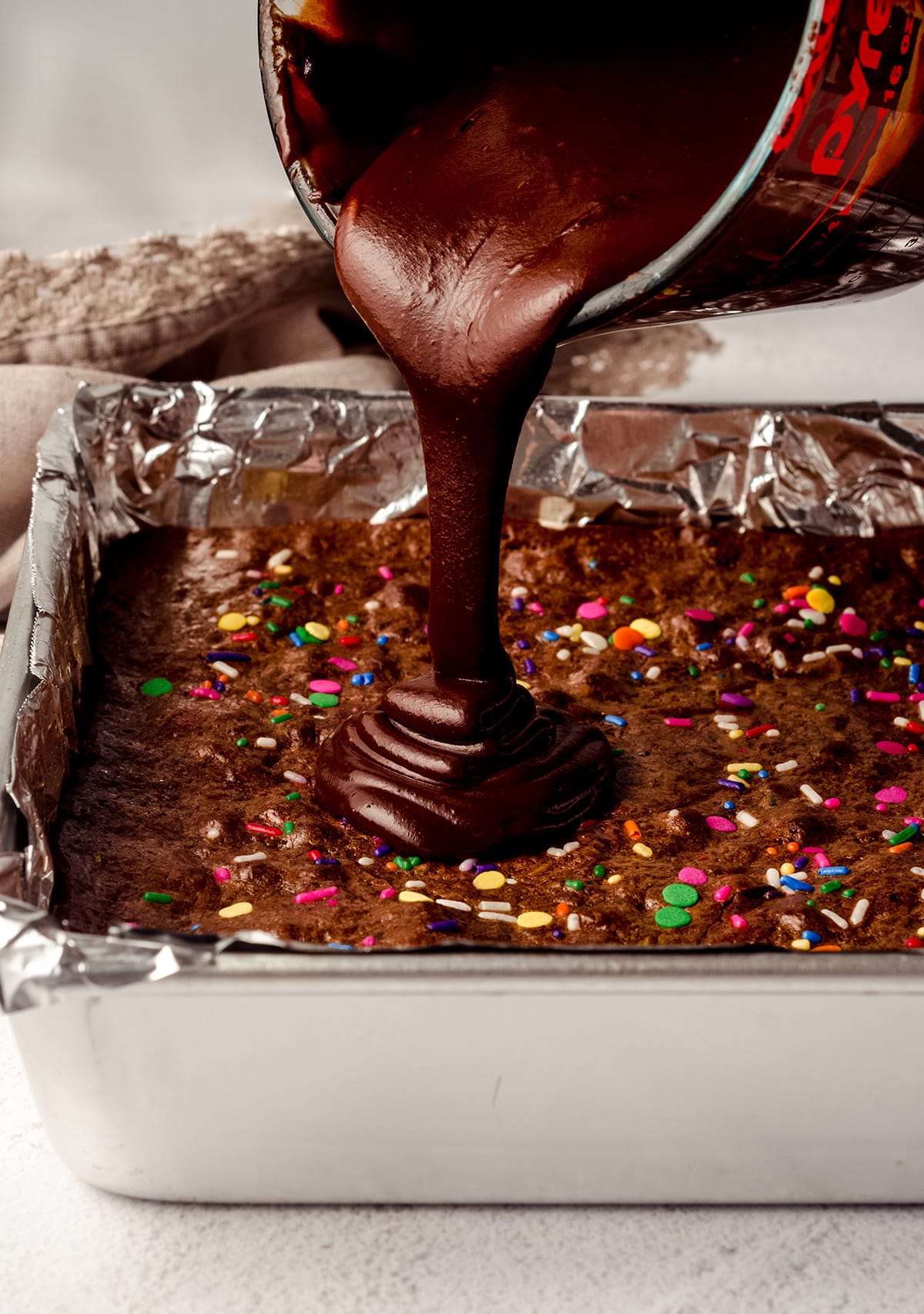 pouring chocolate ganache onto funfetti brownies