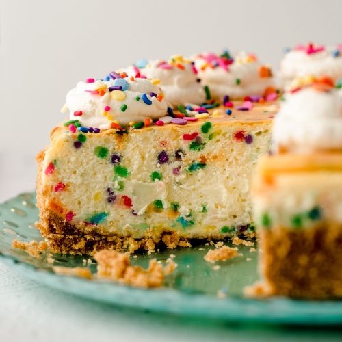 sliced funfetti cheesecake with whipped cream and sprinkles on top