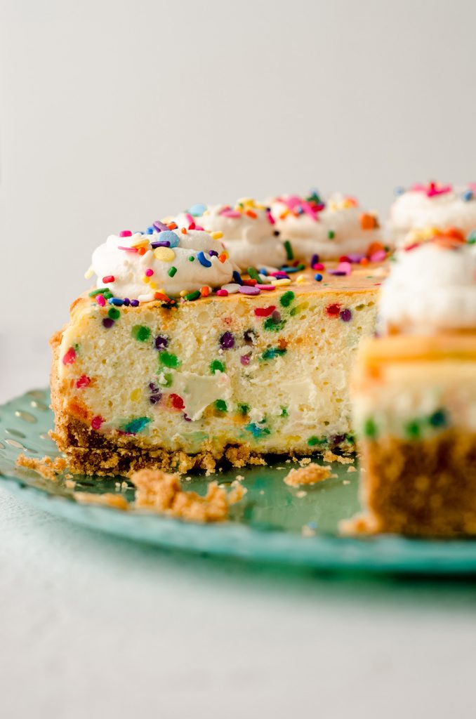 sliced funfetti cheesecake with whipped cream and sprinkles on top