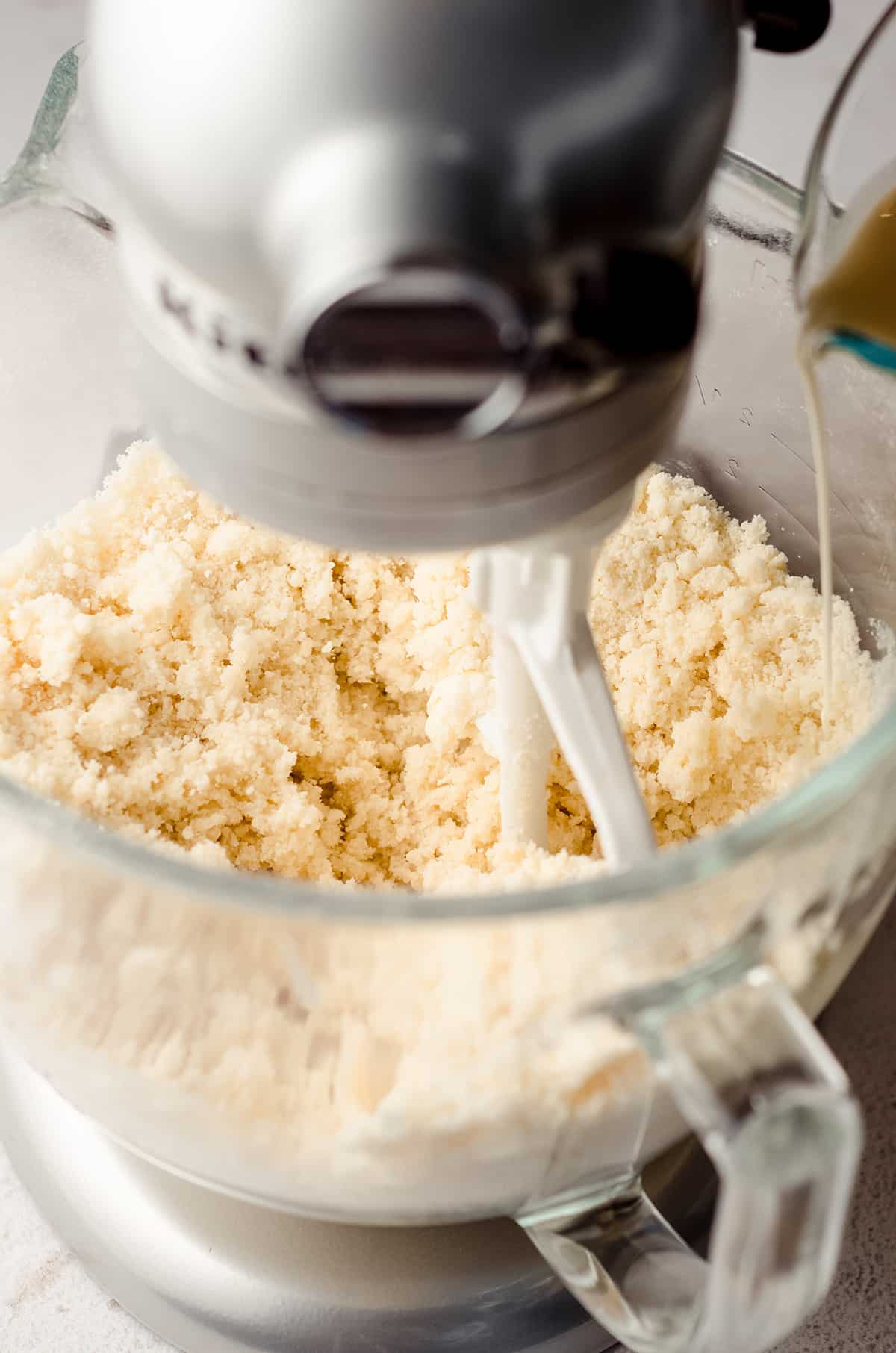 pouring heavy cream into white cake batter in the bowl of a mixer