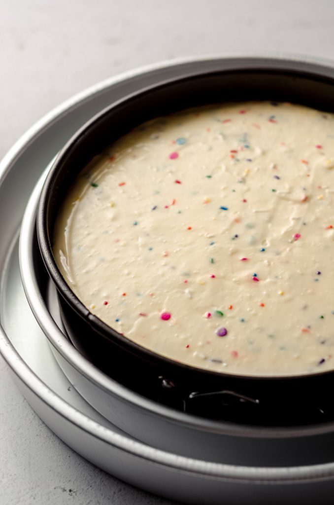 funfetti cheesecake batter in a springform pan and pans prepped for a water bath and ready to bake
