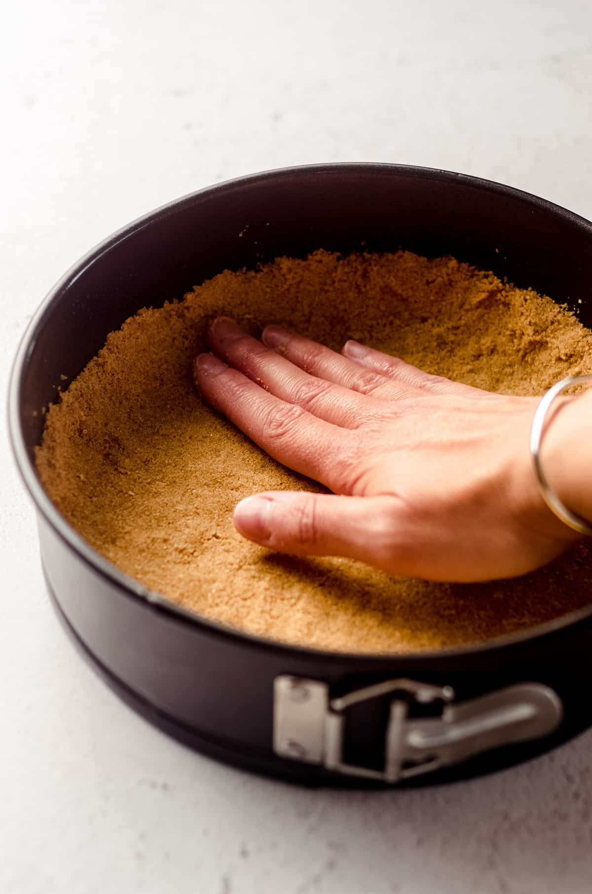 hand pressing a graham cracker crust into the bottom of a springform pan