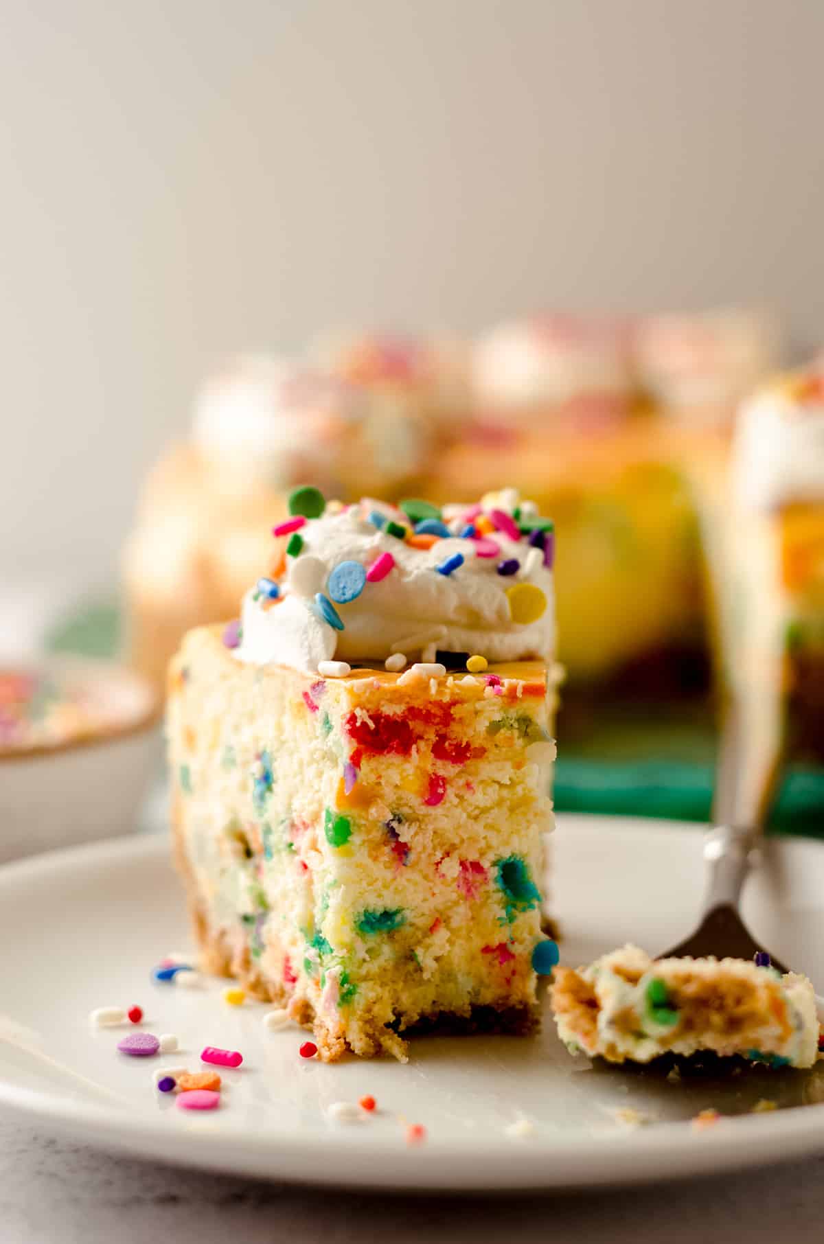 funfetti cheesecake slice on a plate with a bite taken out of it