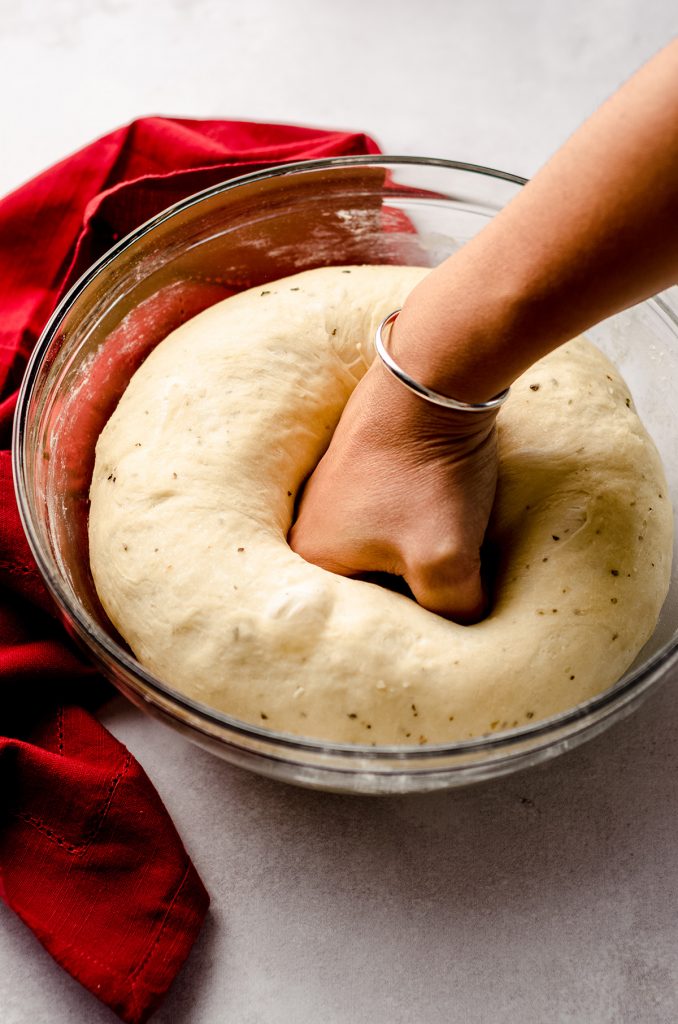 fist punching down pizza pull apart bread dough in a glass bowl