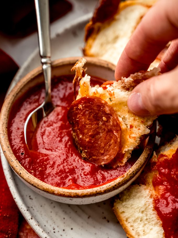 Someone is dipping a slice of pizza pull-apart bread into a bowl of sauce.