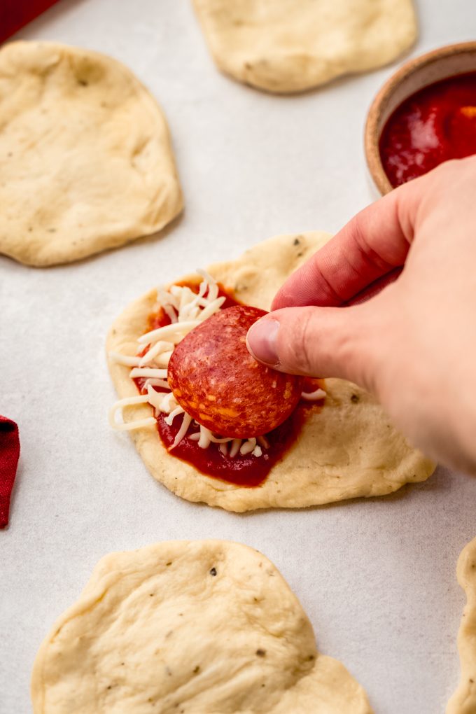 Someone is placing a slice of pepperoni on a disc of dough for pizza pull-apart bread.
