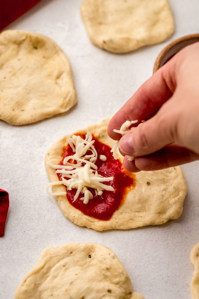 Someone is sprinkling shredded cheese on a disc of dough for pizza pull-apart bread.