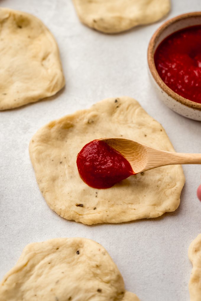 Someone is using a wooden spoon to put pizza sauce on a disc of dough for pizza pull-apart bread.