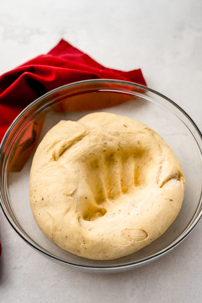 A ball of yeasted dough that has been punched down after rising and you can see the imprint of a fist in it.