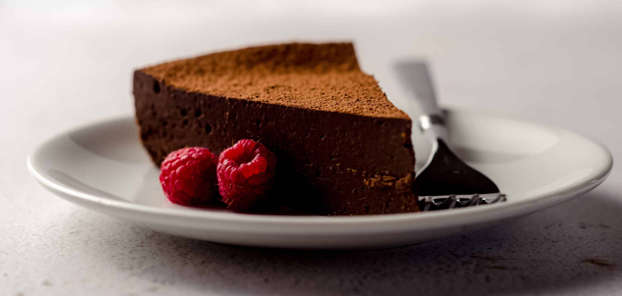 slice of gluten free dairy free cake on a plate with raspberries and a fork