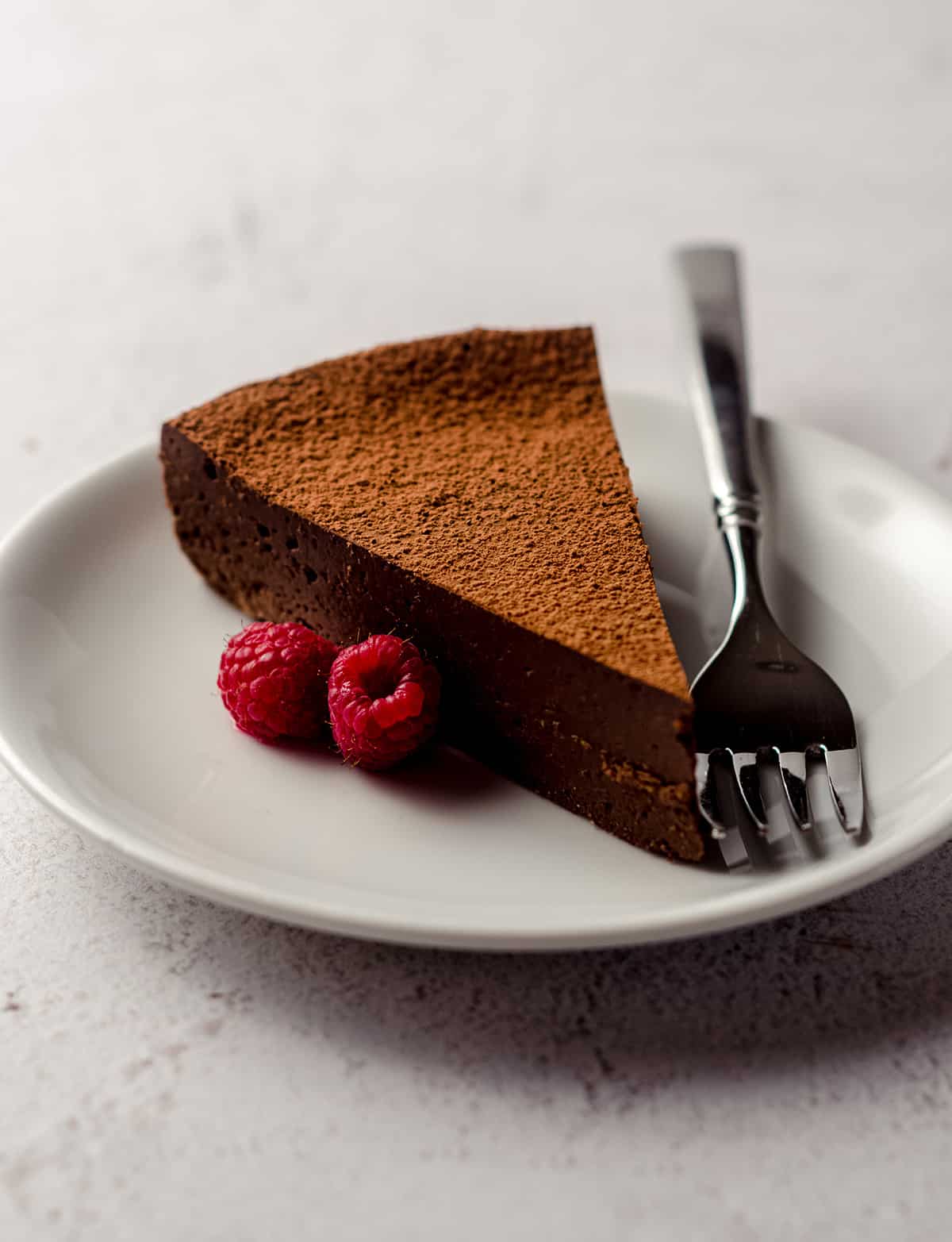 slice of gluten free dairy free cake on a plate with raspberries and a fork