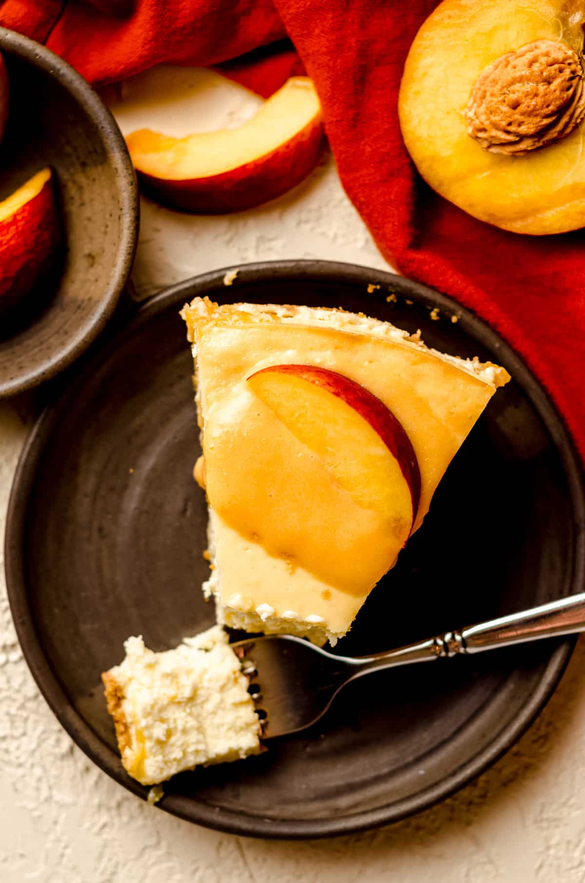 aerial photo of slice of peach cheesecake topped with peach curd and a peach slice on a plate with a fork