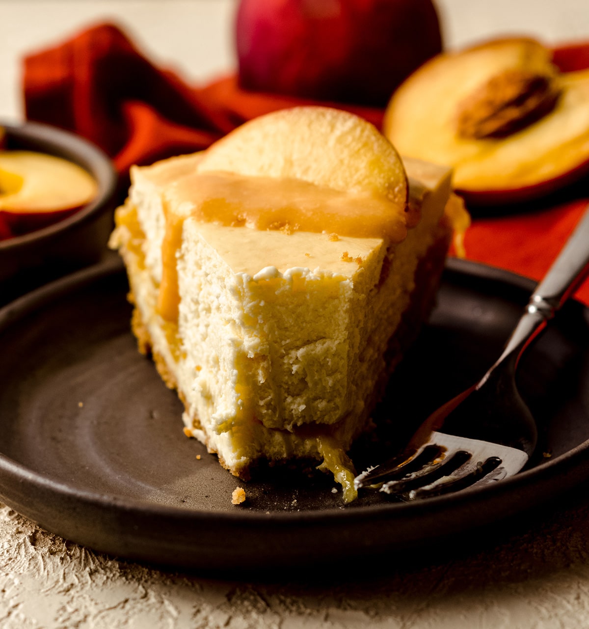 slice of peach cheesecake topped with peach curd and a peach slice on a plate with a fork