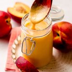 a spoon pulling a scoop of peach curd out of a jar